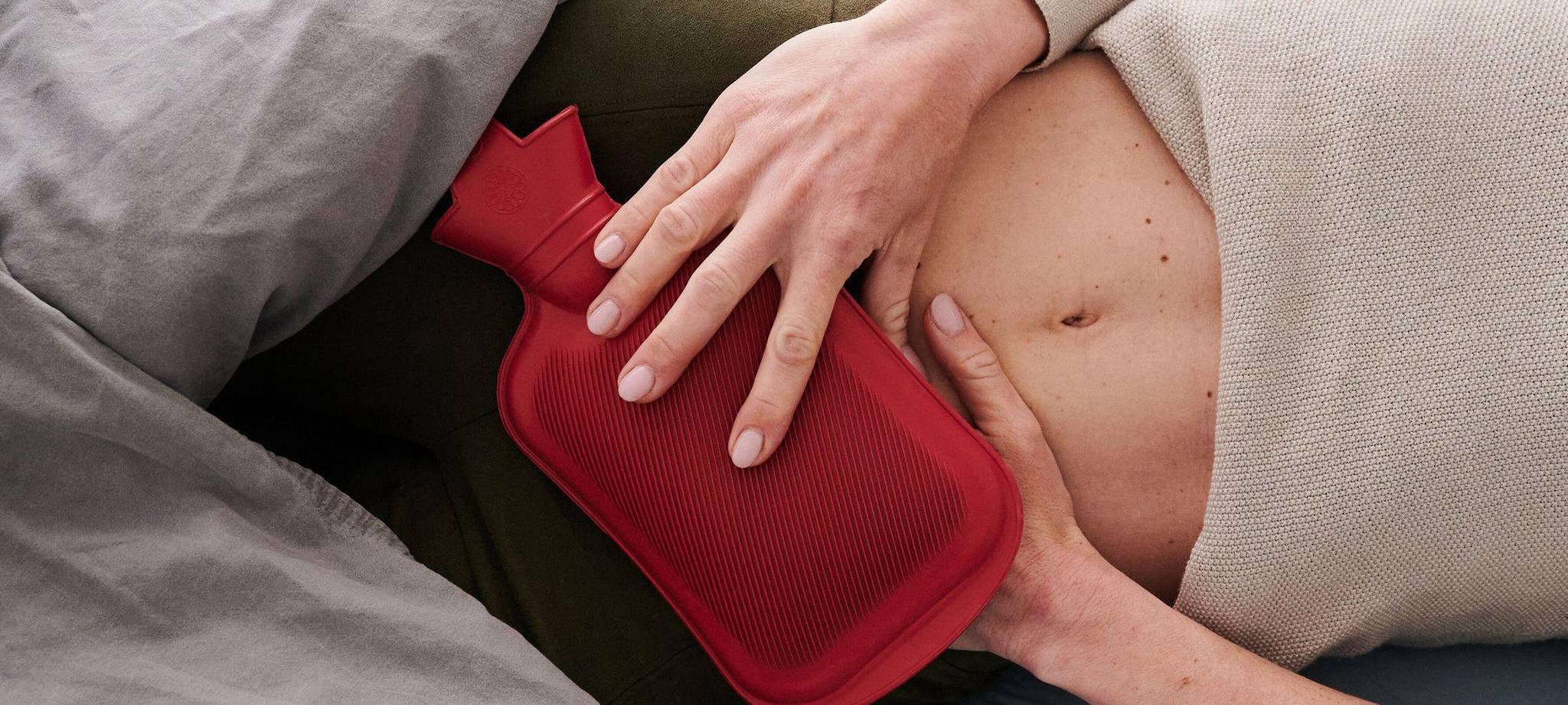 Frau hält sich eine Wärmflasche an den Unterbauch