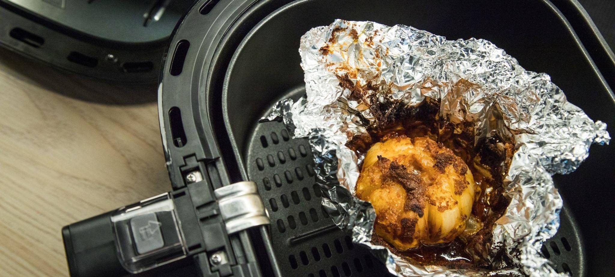 Eine in Alufolie gewickelte Zwiebel liegt in einem Airfryer