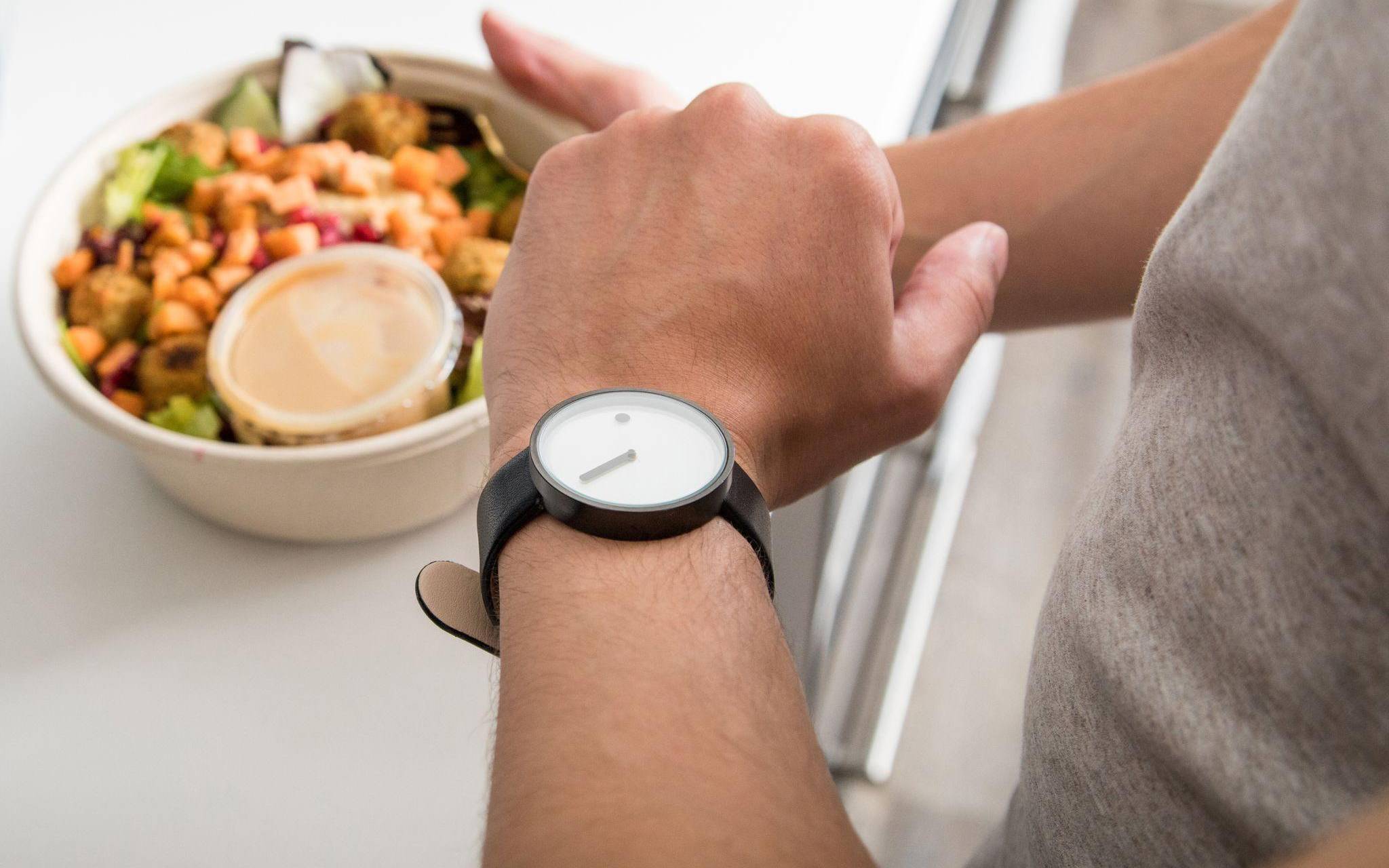 Ein Mann mit einem Teller in der Hand sieht auf seine Uhr