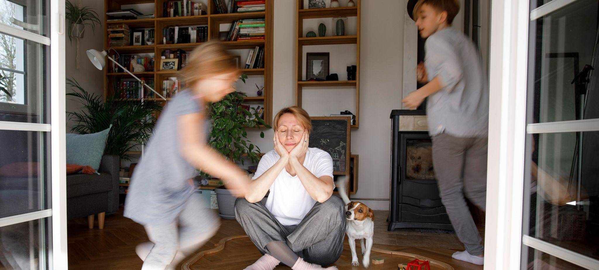 Gestresste Mutter sitzt zwischen dem Spielzeug ihrer Kinder