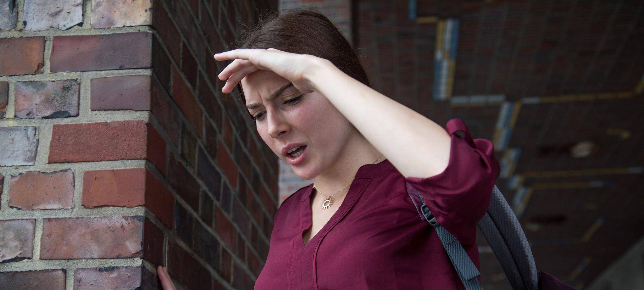 Frau stützt sich an einer Wand ab, weil ihr schwindelig ist