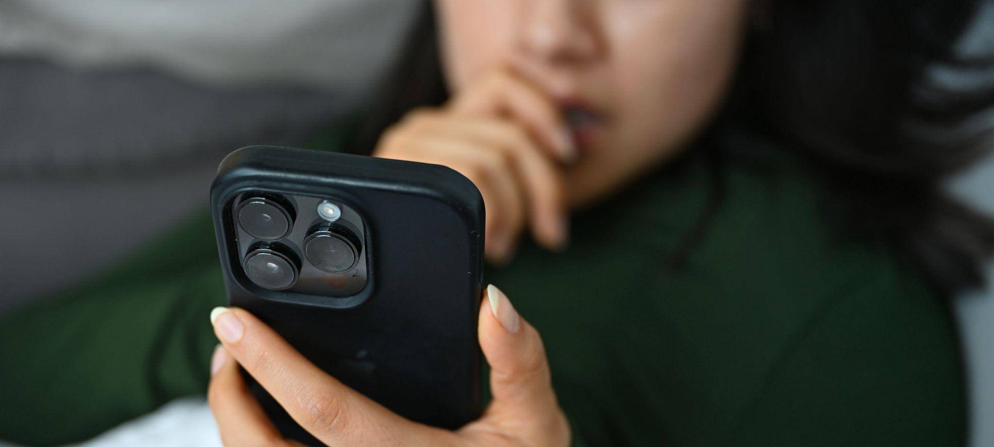 Eine junge Frau liegt mit ihrem Handy auf der Couch