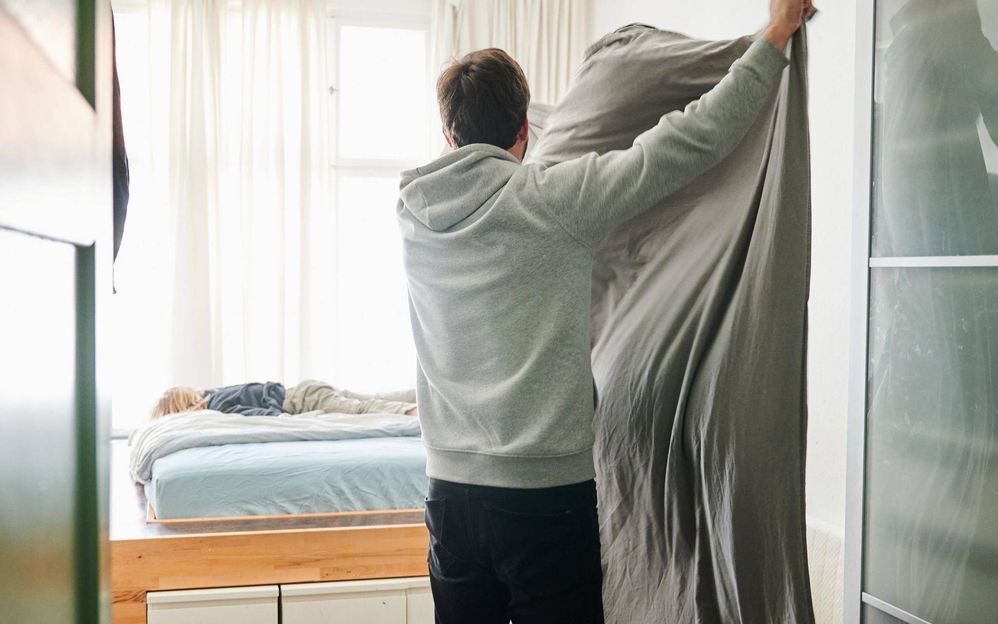 Ein Mann bezieht das Bett und schüttelt dabei eine Bettdecke