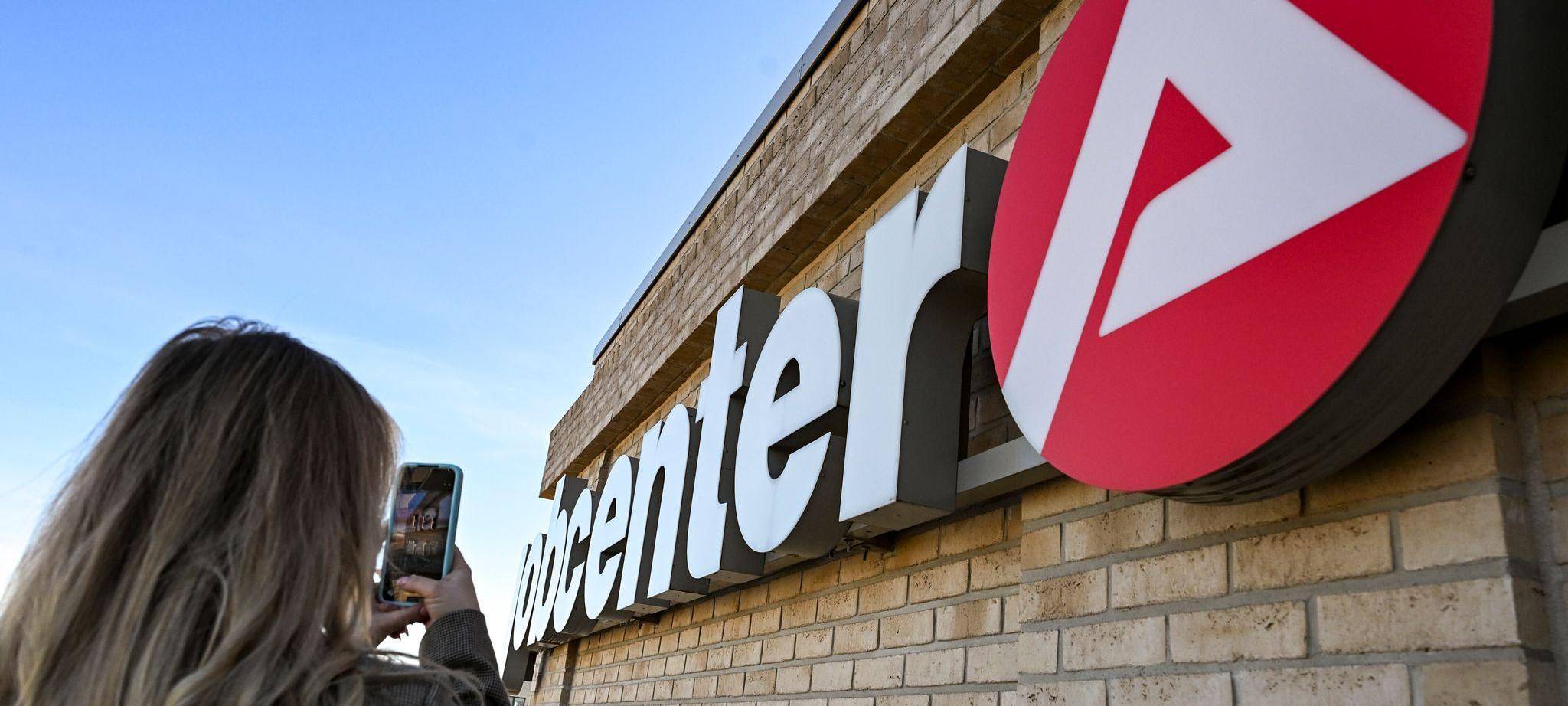 Eine junge Frau fotografiert das Logo eines Job Centers